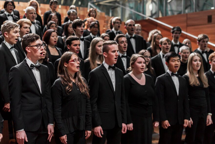 Large choir standing in rows singing, wearing formal black suits and dresses.