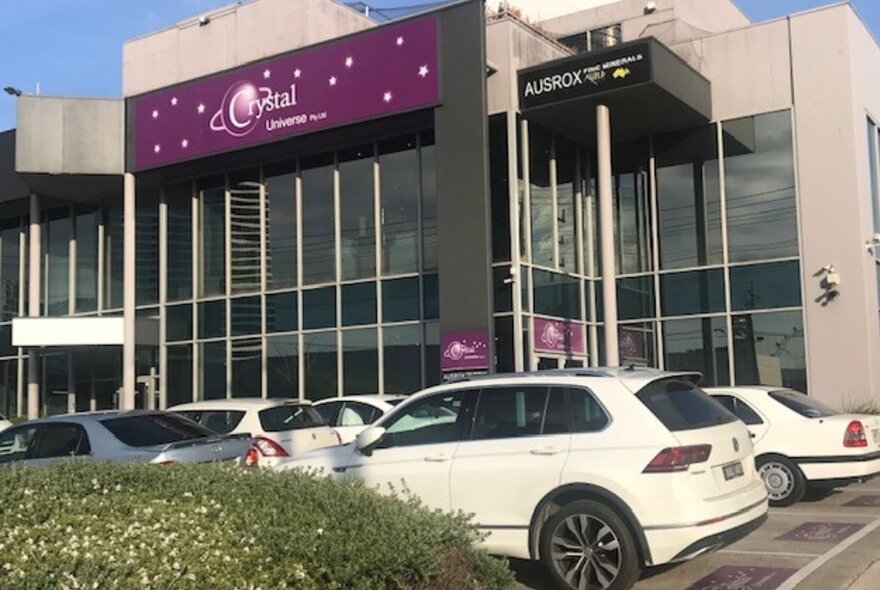 The shopfront of Crystal Universe, with white cars in the foreground, tall windows and purple signage.