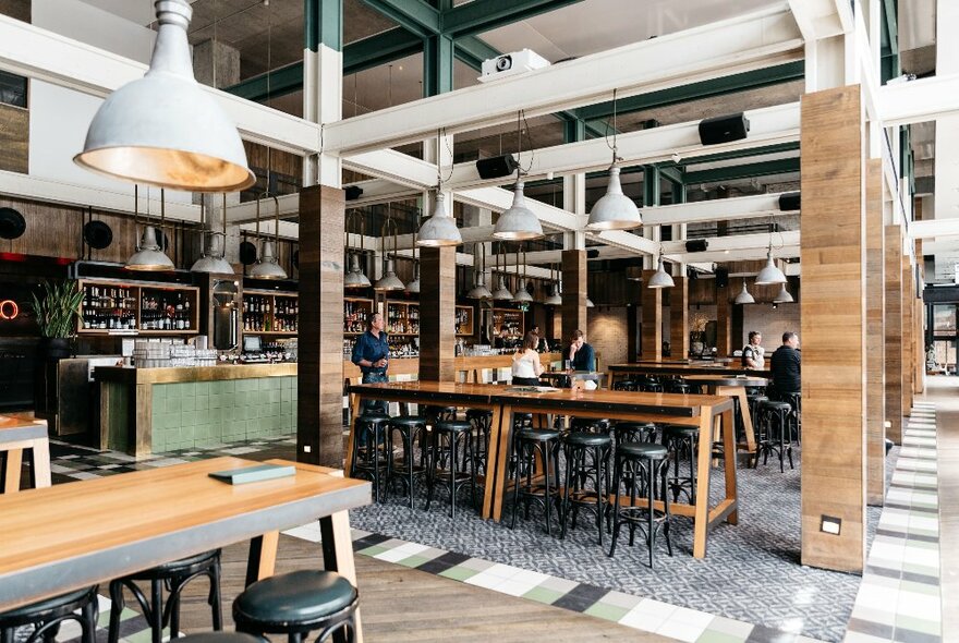 Industrial interior of a large casual restaurant and bar with high tables and large lights hanging down. 