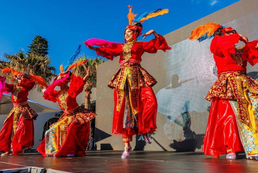 An Asian dance troupe dressed in red and gold performing on a stage.