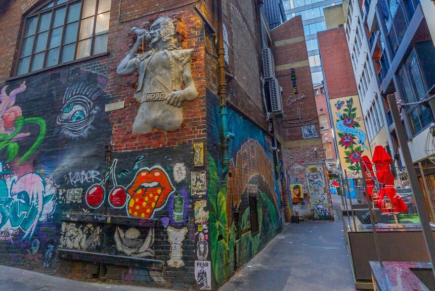 A sculpture of a singer on a brick wall surrounded by street art.