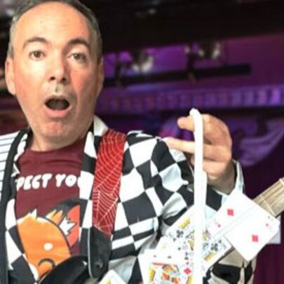 Magician-musician holding a guitar with playing cards attached to the neck.