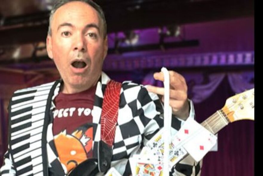 Magician-musician holding a guitar with playing cards attached to the neck.