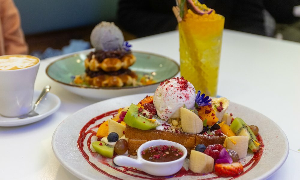 A colourful French toast dish with fruit, a plate of waffles and a drink.