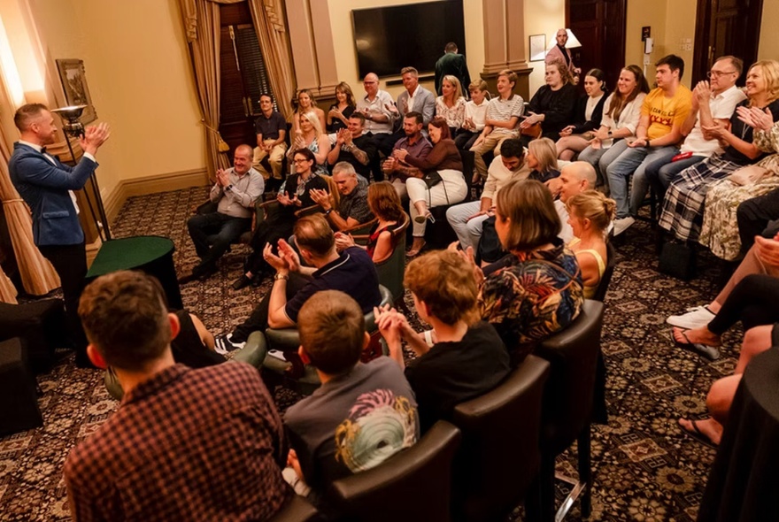 A seated audience in an intimate theatre setting watching a magician perform.