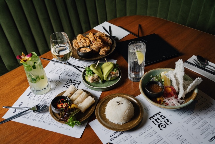 Overhead view of a wooden dining table with several plates of food and drinks resting on large paper menus.