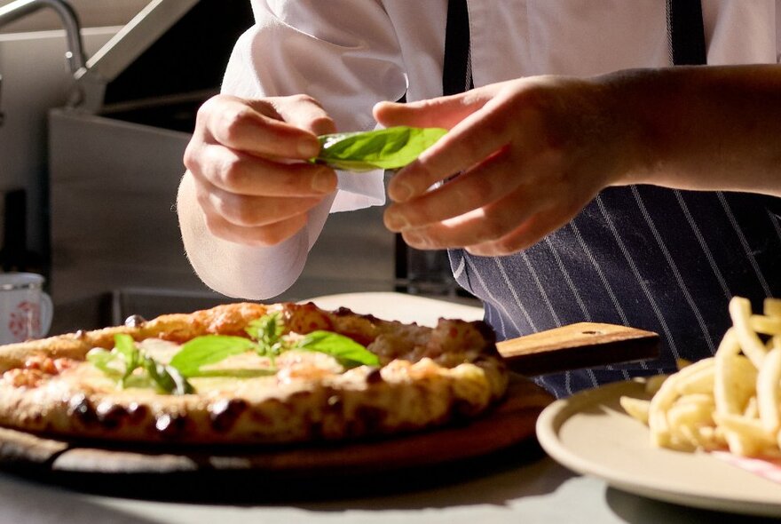 A chef putting the finishing touches onto a pizza, next to a plate of fries.