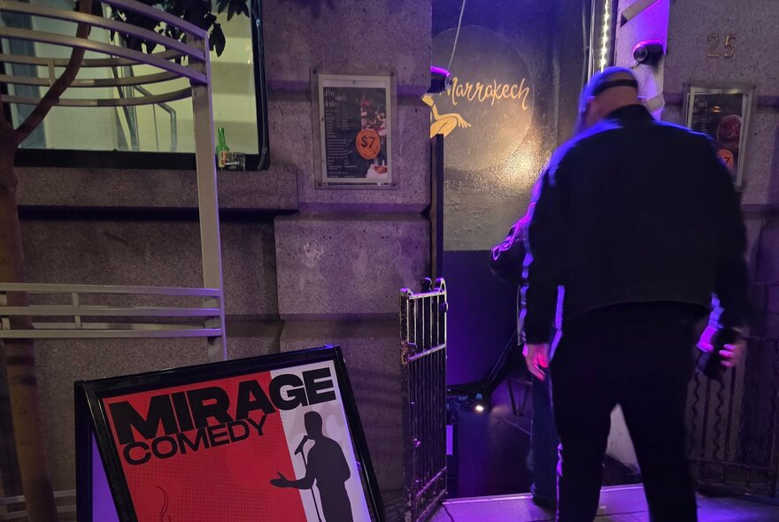 A man walking into a downstairs venue next to an advertising board.