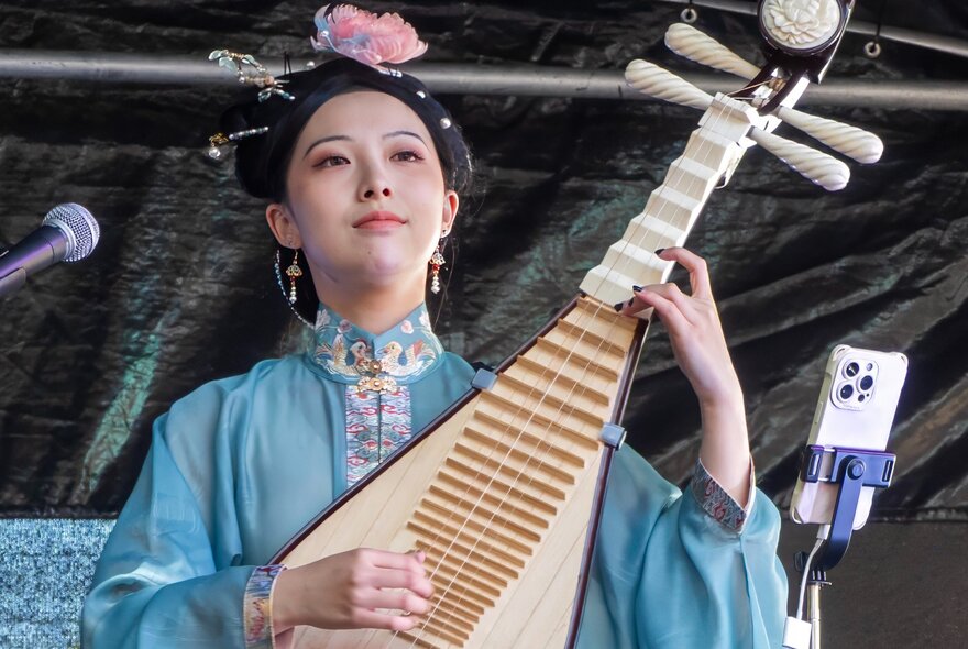 A musician in traditional Asian dress playing a four-stringed Chinese lute, or Pipa.