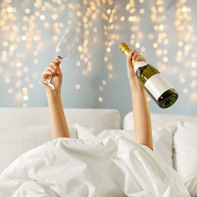 Person in bed holding up champagne and a glass.