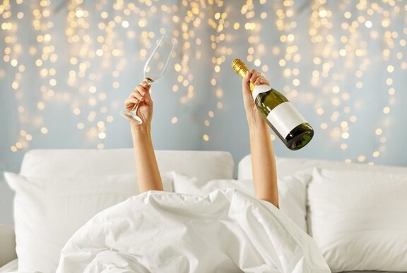 Person in bed holding up champagne and a glass.