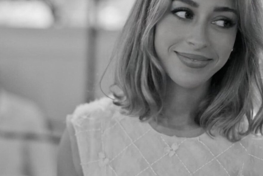 Singer Jemma Cher, with shoulder-length blonde hair, wearing embroidered white sleeveless dress.