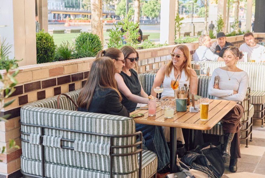 A group of friends enjoying a drink in a booth seat at an outdoor terrace bar.