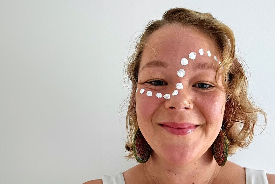 A woman with Indigenous dot painting on her face, smiling. 