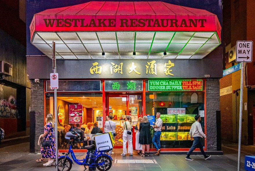 A group of people are standing outside a leon-lit Chinese restaurant