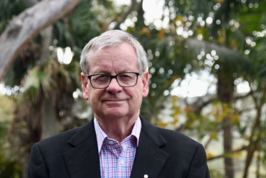 Reporter, journalist and author Chris Masters, a middle-aged man wearing a shirt, suit jacket and glasses and standing outside with trees in the background.