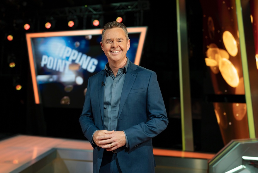 Game show host Todd Woodbridge smiling on the studio set of the TV show Tipping Point.
