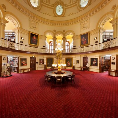 Historic Supreme Court Library interior with red carpet, arched mezzanine story, domed ceiling, stacks of library shelves and portraits.