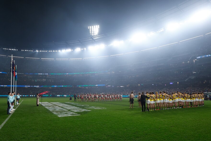 Misty lights on the oval as AFL football players line up before a game.