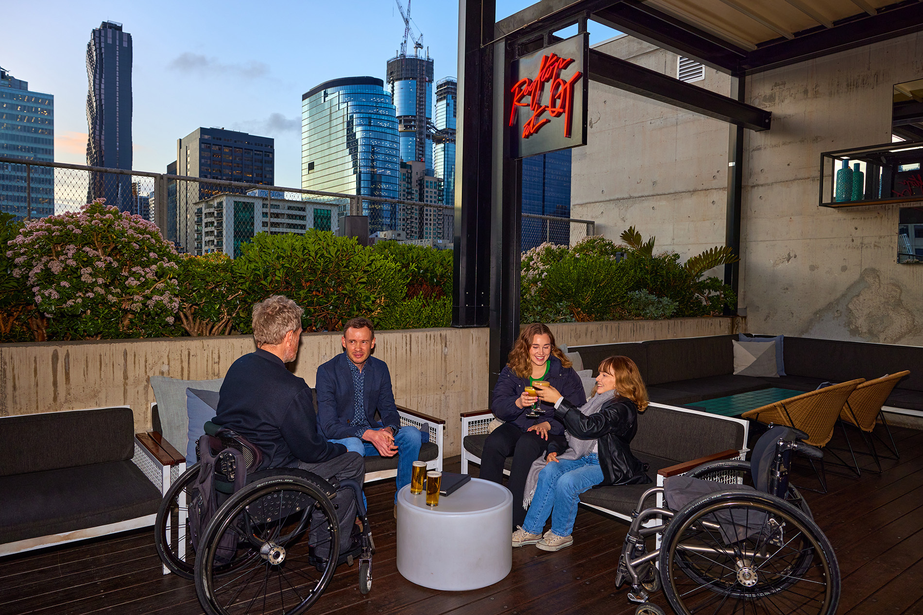A group of friends drinking on a rooftop bar, two are using wheelchairs.
