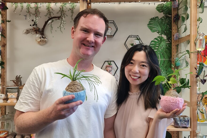 A man and a woman looking happy holding up a kokedama ball each. 