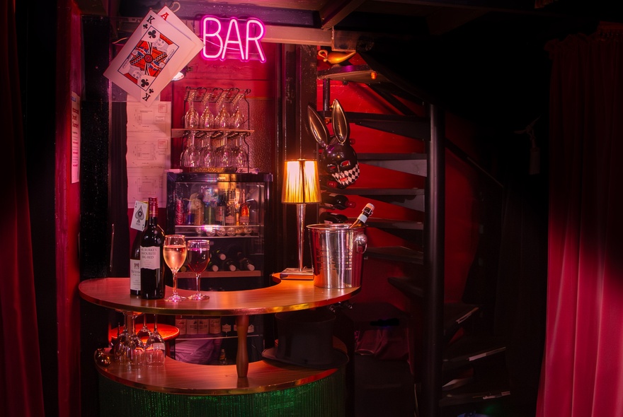 A dimly lit bar with a pink neon sign that says 'bar' inside a small venue.
