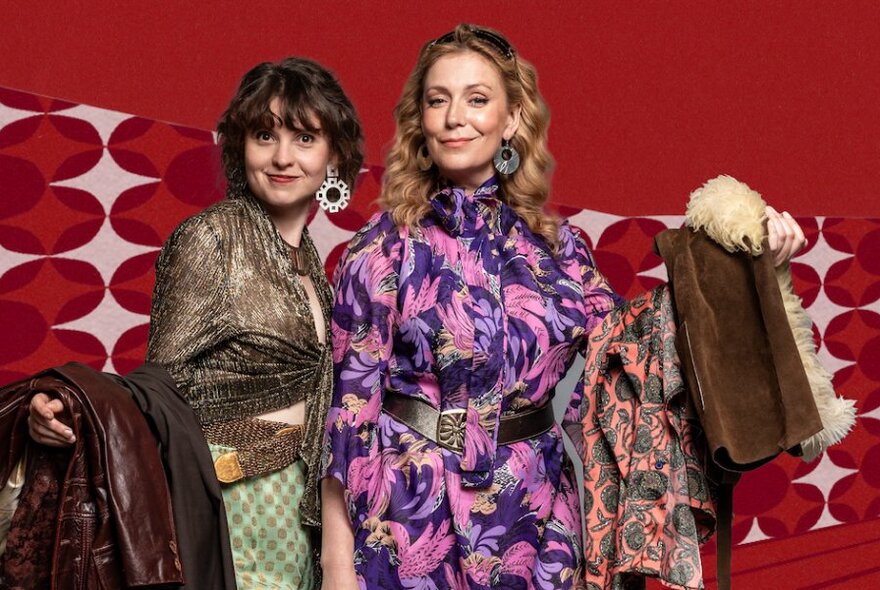 Two women dressed up in patterned clothes and looking smug against a red background. 