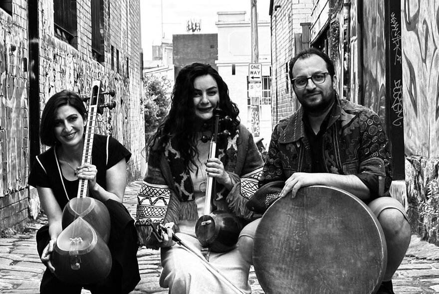 A black and white image of three sufi musicians and their instruments in an alleyway. 