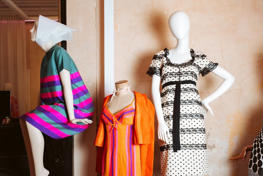 Three faceless mannequins wearing bold and brightly coloured dresses.