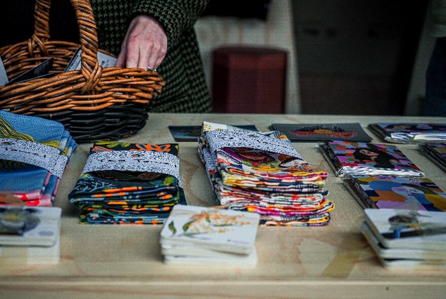 Close up of brighlty-coloured folded, fabric, hands near a basket at left-rear. 