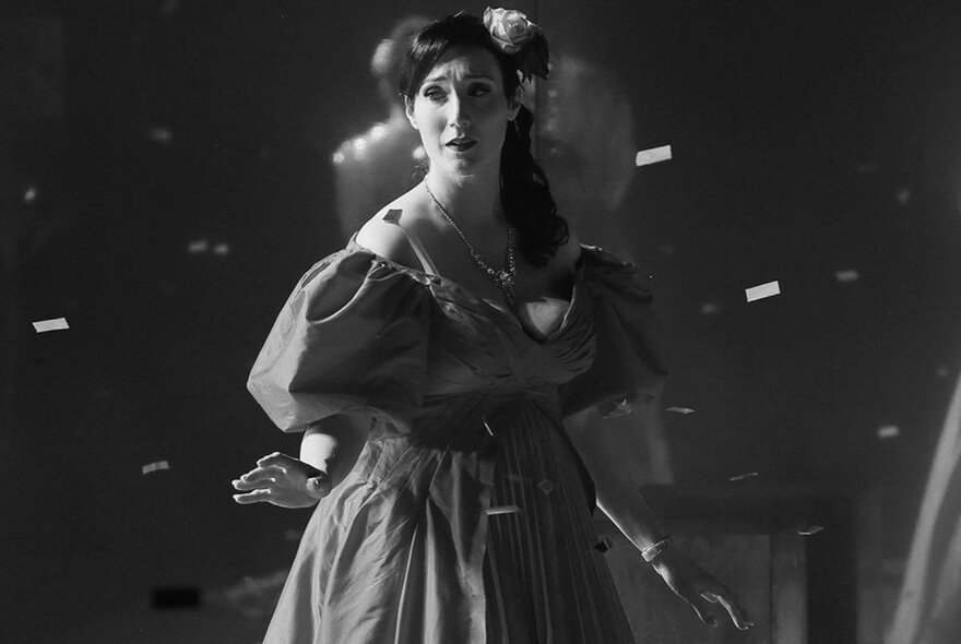 A black and white image of a woman in a formal ballgown performing. 