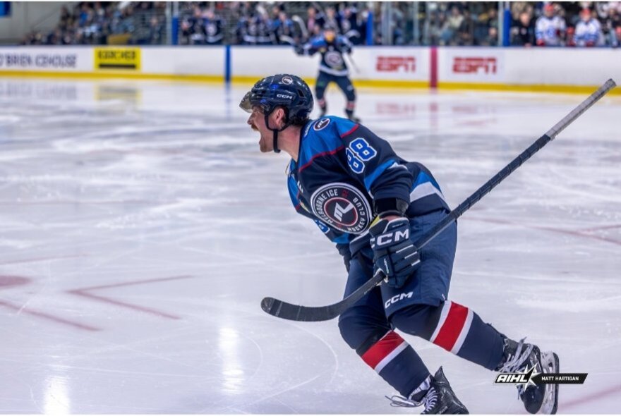 An ice hockey player in blue, skating on an ice hockey rink.