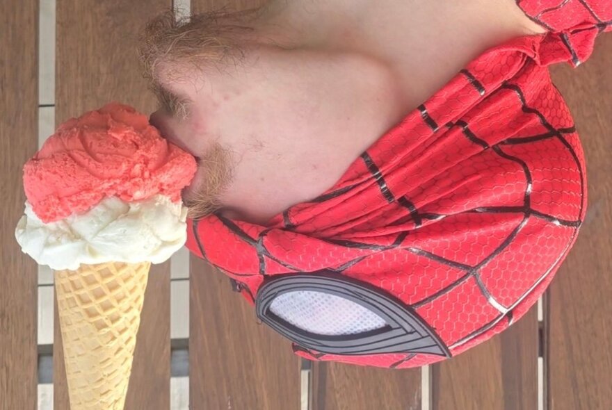 Man wearing Spiderman hat eating an ice cream upside-down.