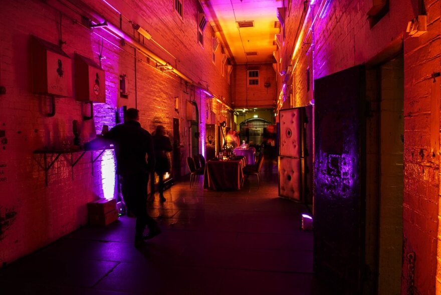 The interior of Old Melbourne Gaol in warm reddish light, with a long dining table in the back are and people seated around it.