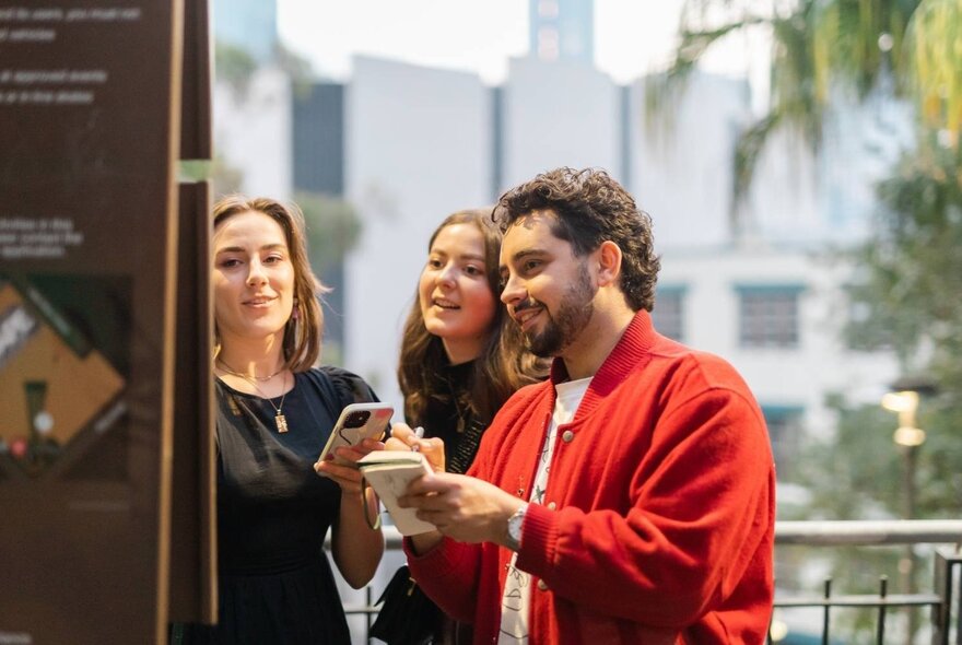 A group of people looking at a sign or map outdoors, interacting with their smartphones.
