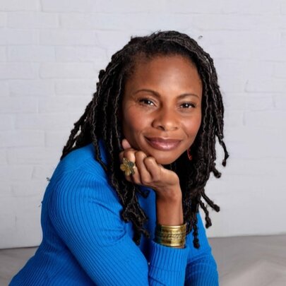A woman in a cobalt blue top smiles serenely with her chin resting on her hand. 