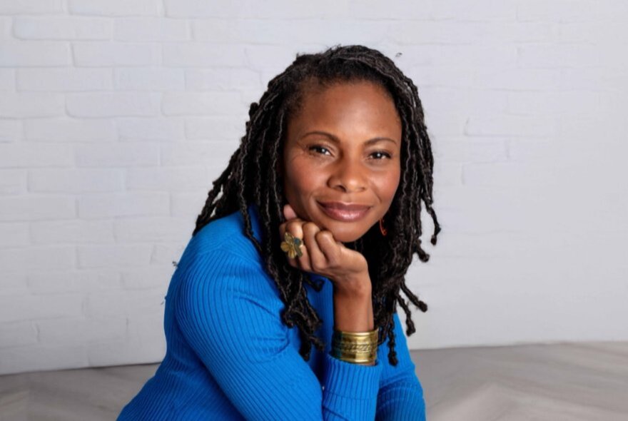 A woman in a cobalt blue top smiles serenely with her chin resting on her hand. 