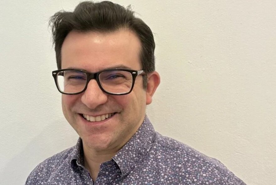Smiling man with dark hair and spectacles.