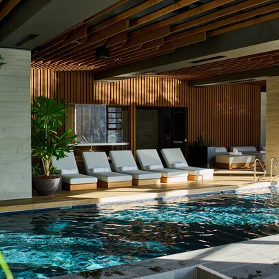 Day beds lined up next to an indoor pool with plants.