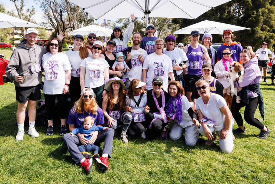 Large crowd gathered in a park with umbrellas, wearing purple scarves and tops.