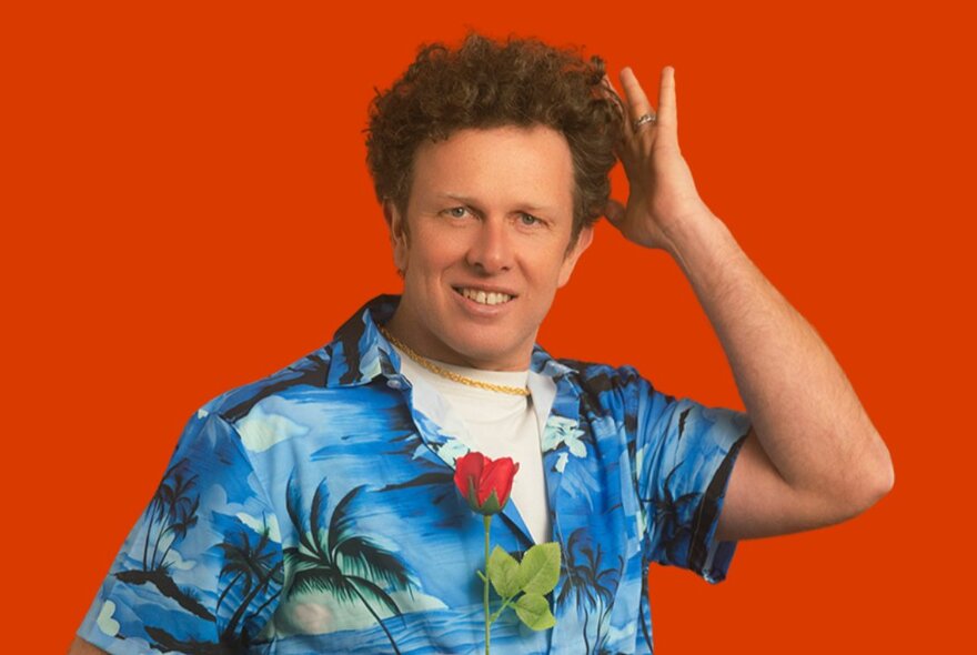 Comedian Nick Capper, a middle-aged man with curly brown hair, wearing a Hawaiian shirt and raising his hand to his head.