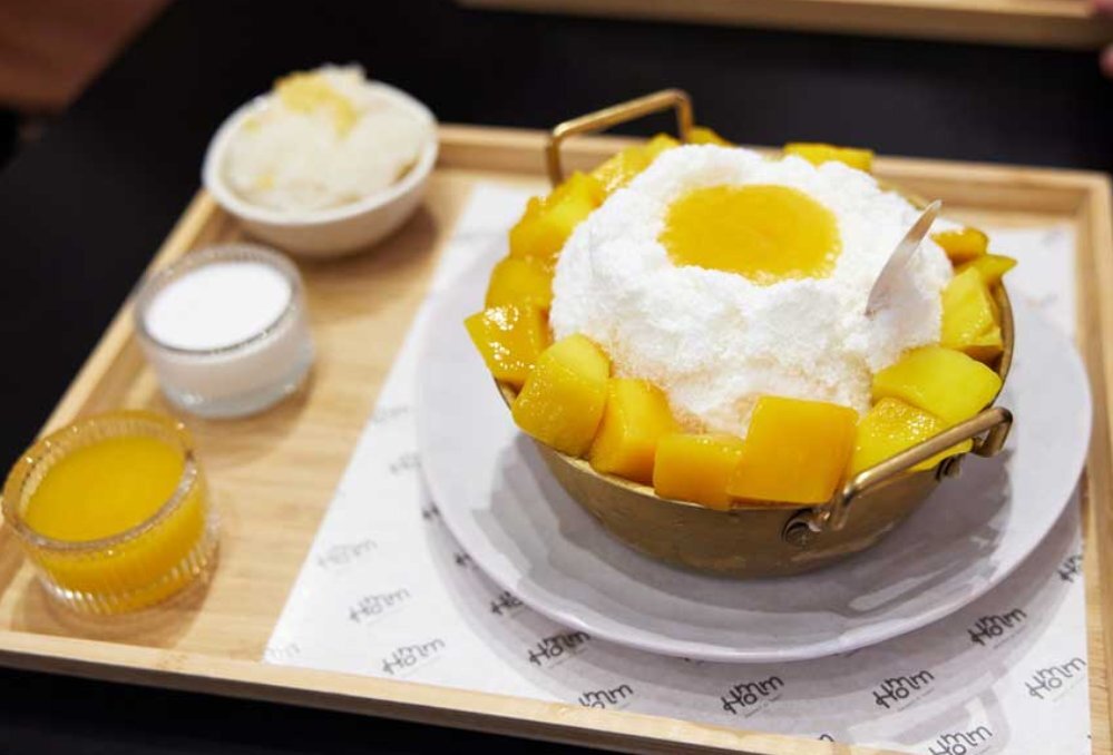 A shaved ice and mango dessert on a wooden tray