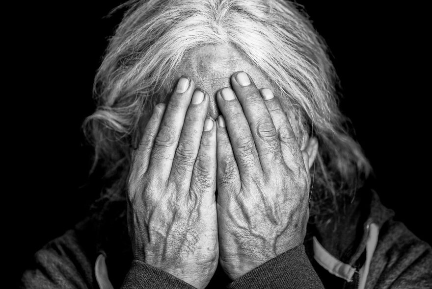 A person with grey hair covering their face with their hands.