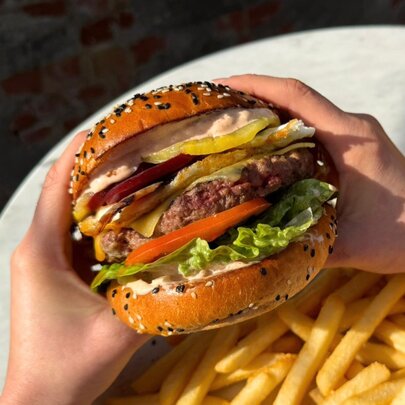 Hands holding up a stacked burger over a plate of fries.
