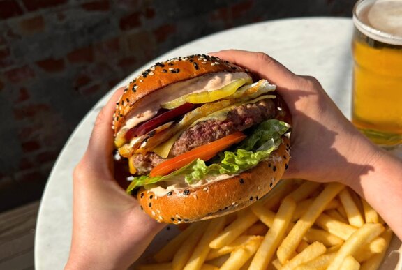 Hands holding up a stacked burger over a plate of fries.