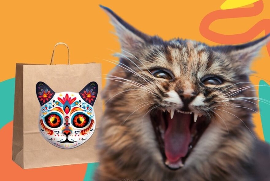 A close-up of a cat hissing while behind it is a brown paper bag with a Day of Dead cat mask painted on the outside of the bag.