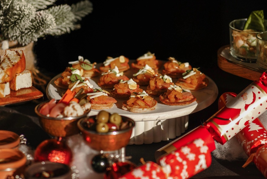 A festive high tea buffet spread on a table, with Christmas bon bon crackers and pine cone decorations.
