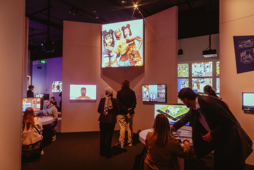 People seated at tables in a game space with screens.