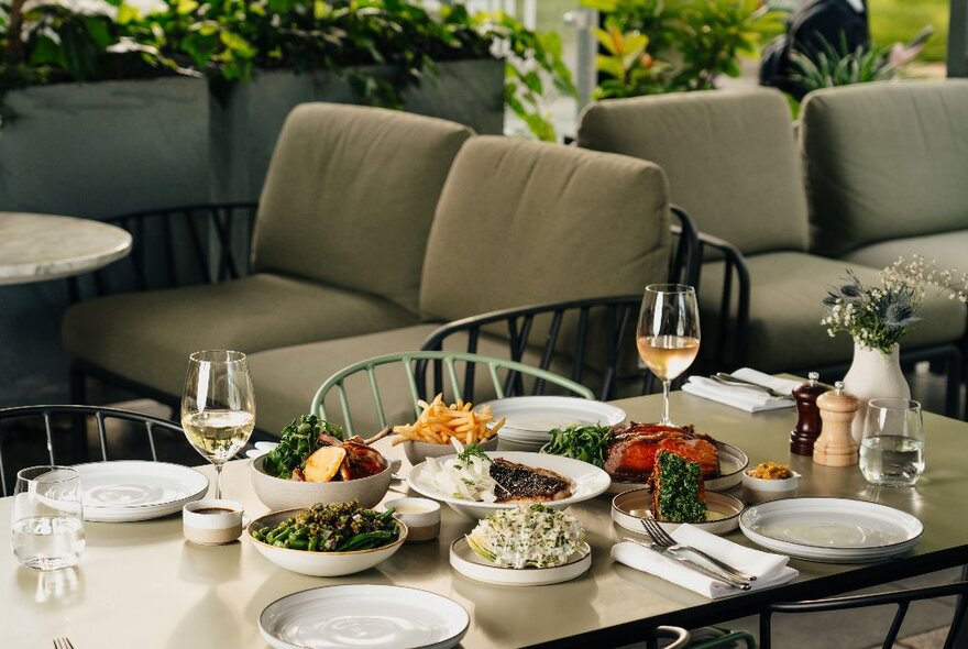 A table at a restaurant laden with gourmet dishes and wine glasses, set for four, with couch seating behind.