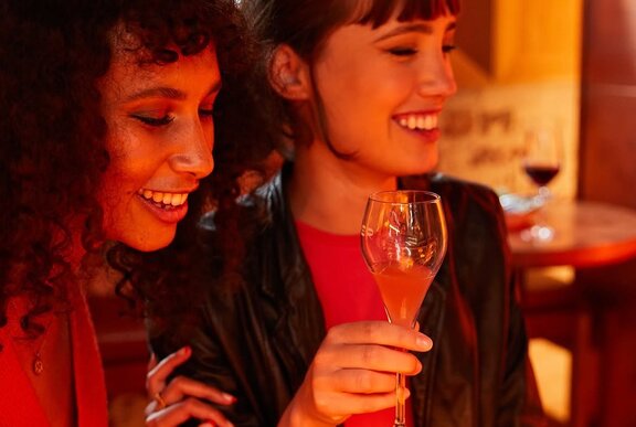People enjoying drinks and toasting with glasses in a warmly lit restaurant setting.